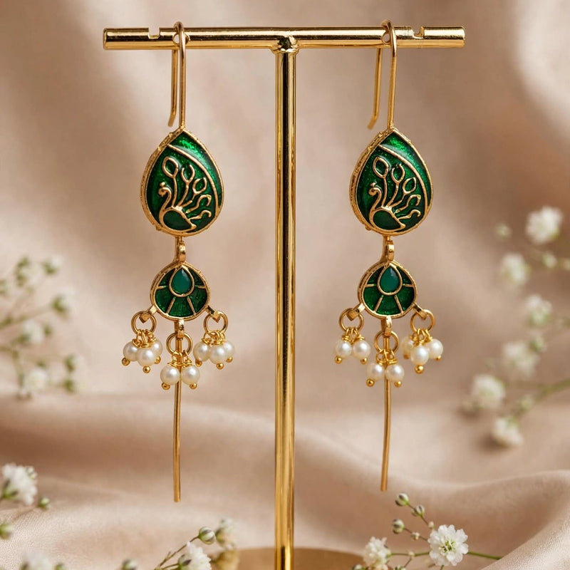 A pair of gold and green traditional Indian earrings displayed on a gold stand, surrounded by small white flowers on a beige fabric background.