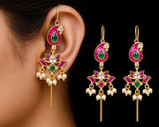 Gold-toned traditional Indian earrings with pink enamel, green stone accents, and white pearl drops, shown worn on an ear and as a pair against a black background.